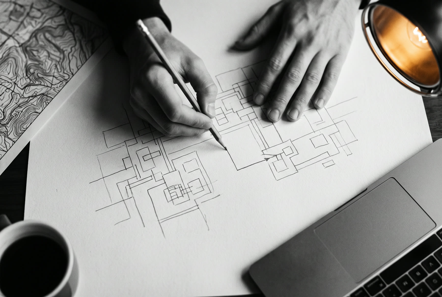 Two hands drawing a route on a large sheet of paper under a desk lamp.