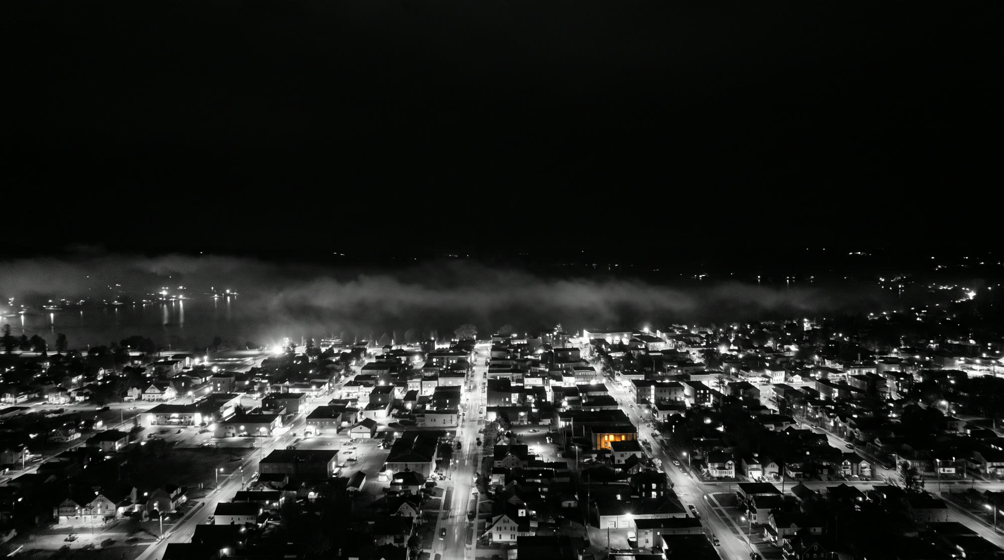 A small lakeside town at night from above, one window lit.