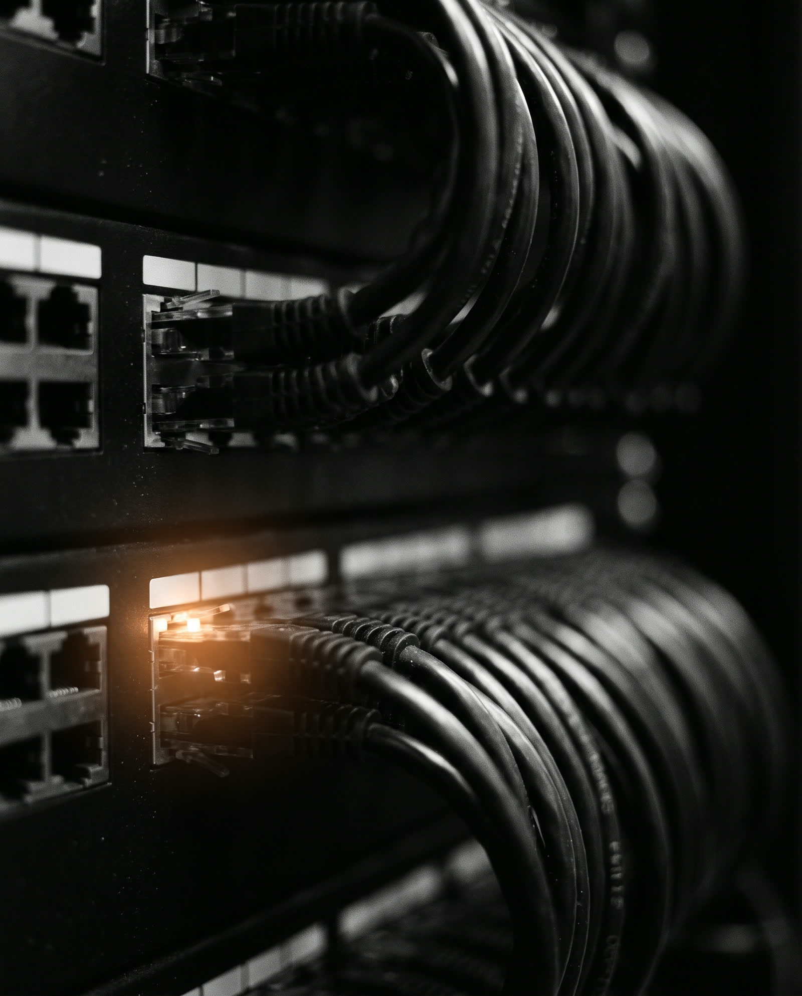 A patch panel in a dark server room with one live cable glowing.
